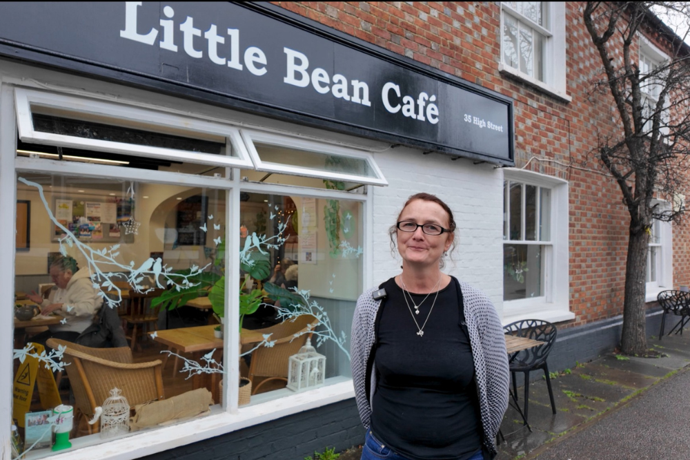 A woman stands outside a small brick-front café called “Little Bean Café