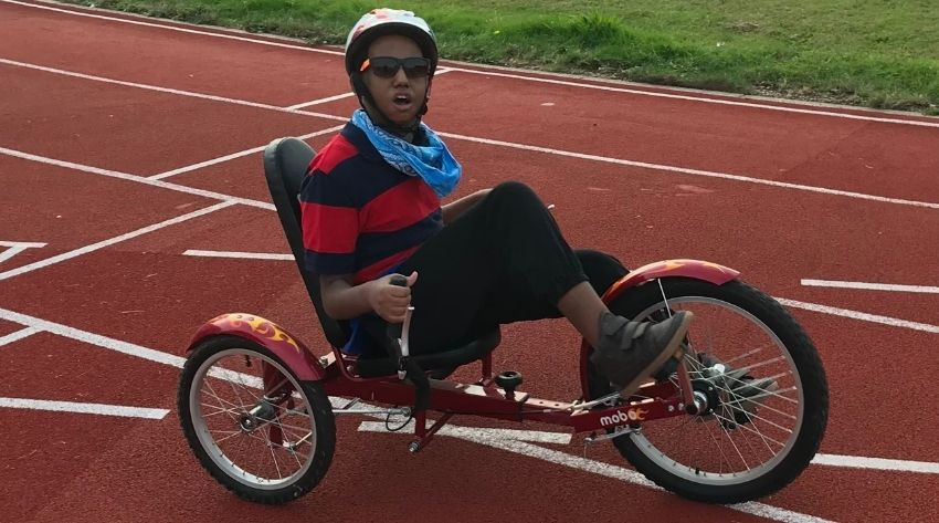 Alazar at a Wheels for All session on a bike wearing a stripy top, bike helmet and sunglasses