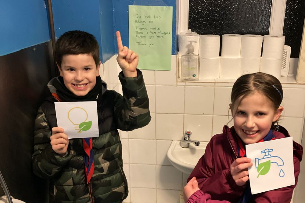 Two young scouts hold up water saving awareness signs where the automatic taps will be installed