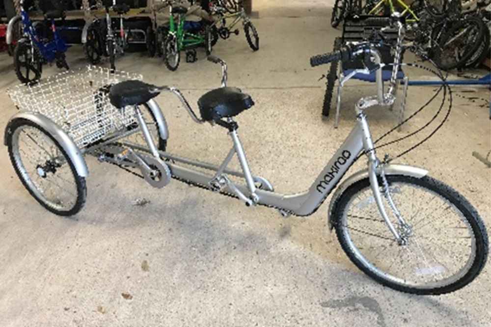 A silver tandem trike with two adjustable height saddles and pedals