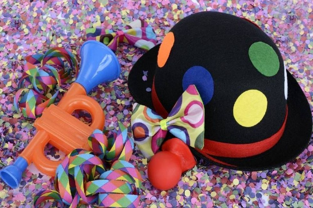 A clown hat, horn and bow tie on a pink background