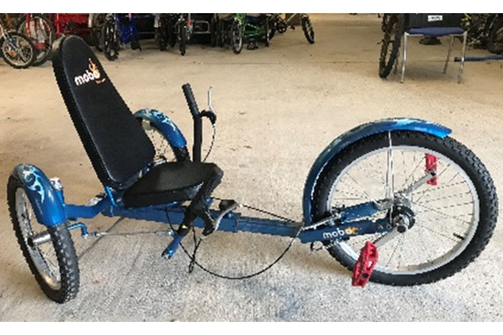 A blue recumbent trike. The ride sits in the seat with backrest and steers with handlebars on either side of the seat. The pedals are on the front wheel of the bike