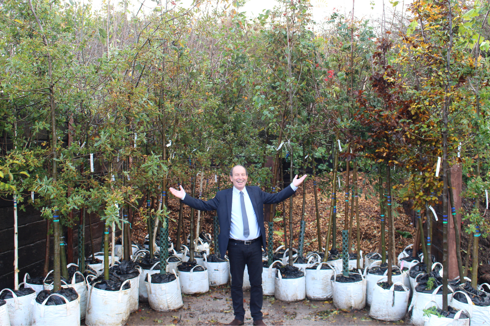 Cllr Roger Noel standing in front of a collection of Queen's Green Canopy tree plants