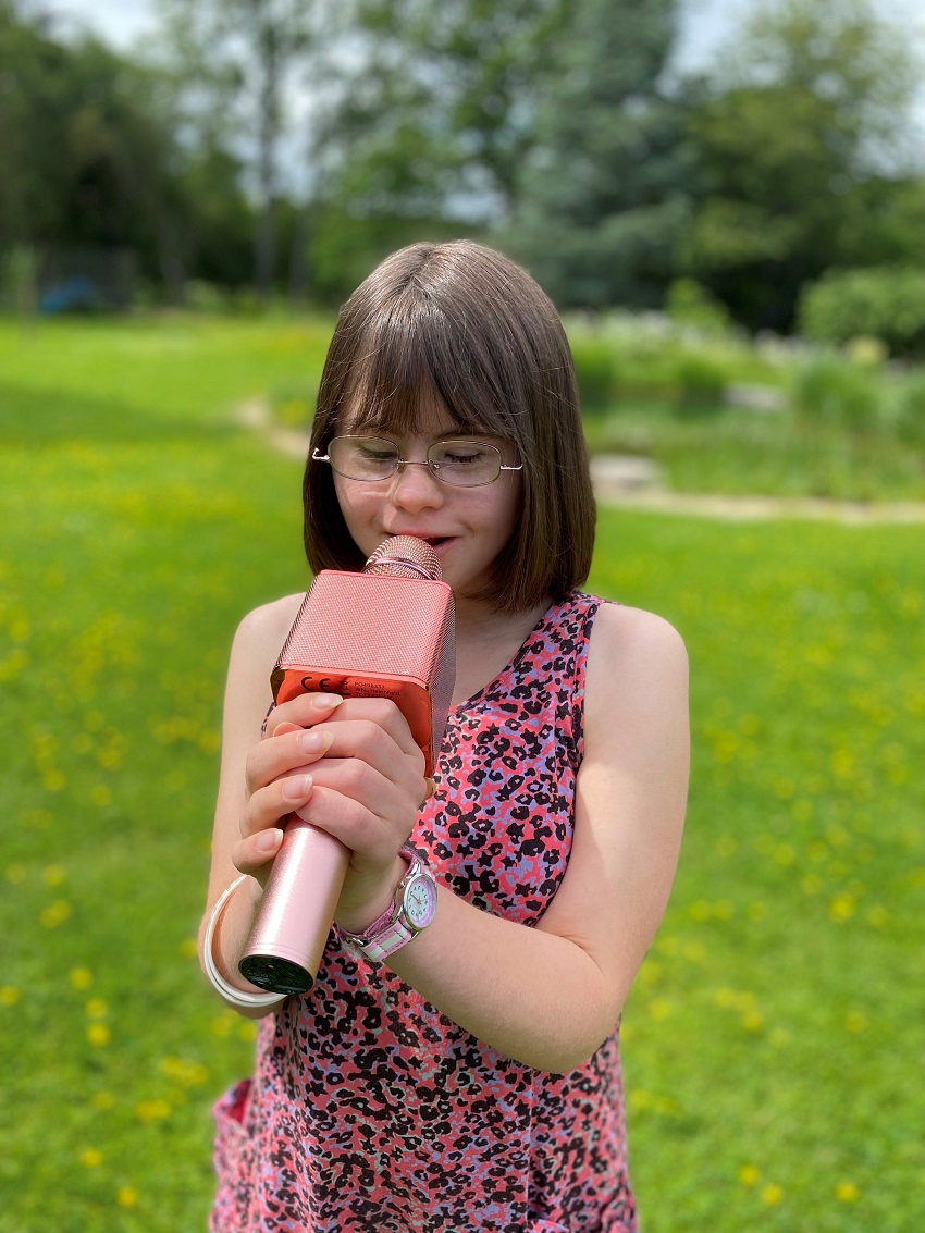 Alice takes part in our karaoke sessions. She's pictured here holding a pink microphone to sing into and is wearing a pink patterned dress