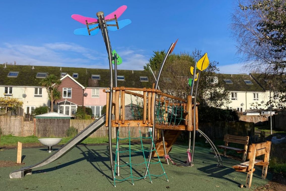 The completed play area has a nature theme with a pink and blue dragonfly on the climbing frame