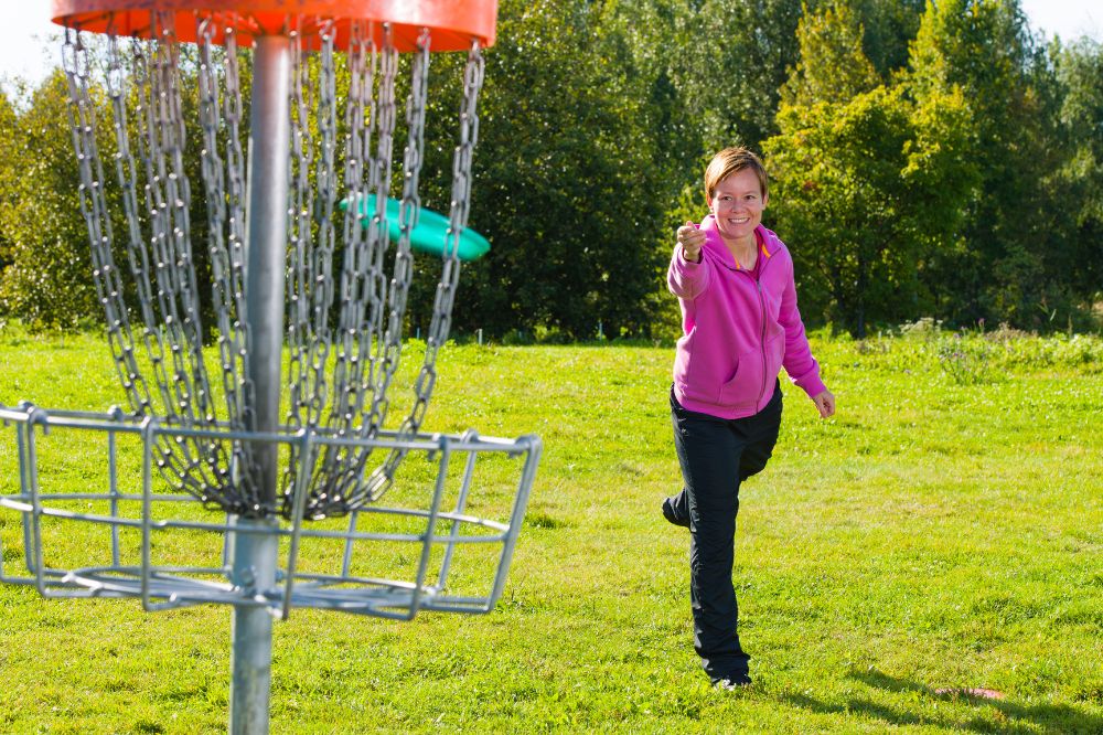 A woman wearing a pink top plays disc golf