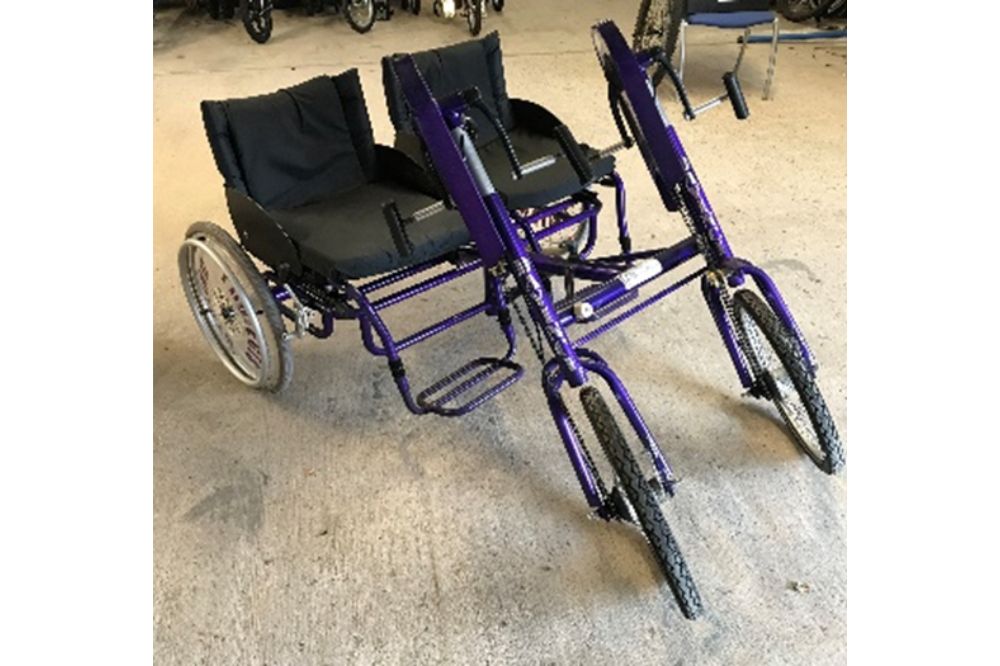 A purple hand-powered tandem trike for two riders in full seats