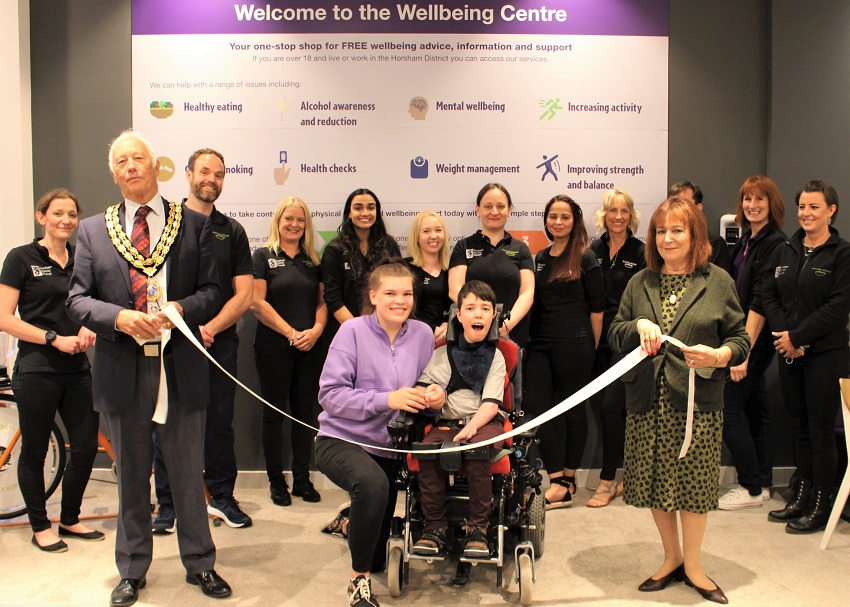 Maddie cuts the ribbon at the new Wellbeing Centre. The ribbon is held by Councillor Claire Vickers and Council Chairman David Skipp. The Wellbeing team stand in a row behind smiling