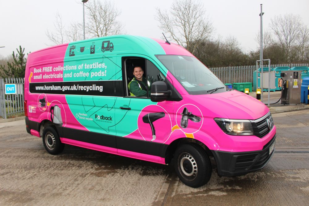A driver smiling in a bright pink and turquoise collection van. The van has Podback and Textiles and electricals collection on the side.